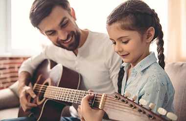 hombre enseñando a una niña a tocar la guitarra