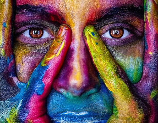 persona con la cara y las manos manchadas de pintura de colores con unos grandes ojos marrones